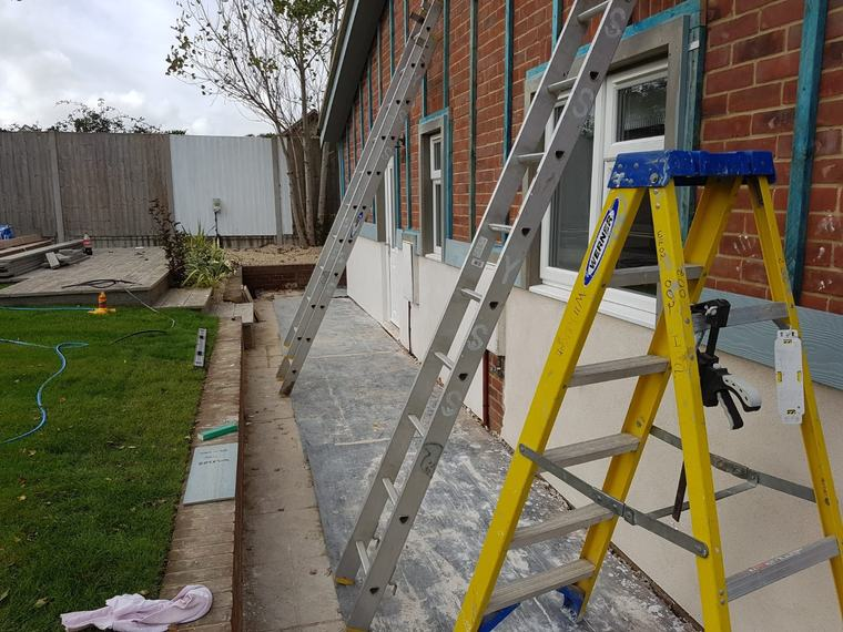 Exterior cladding preparation in progress with ladders, battens and render base
